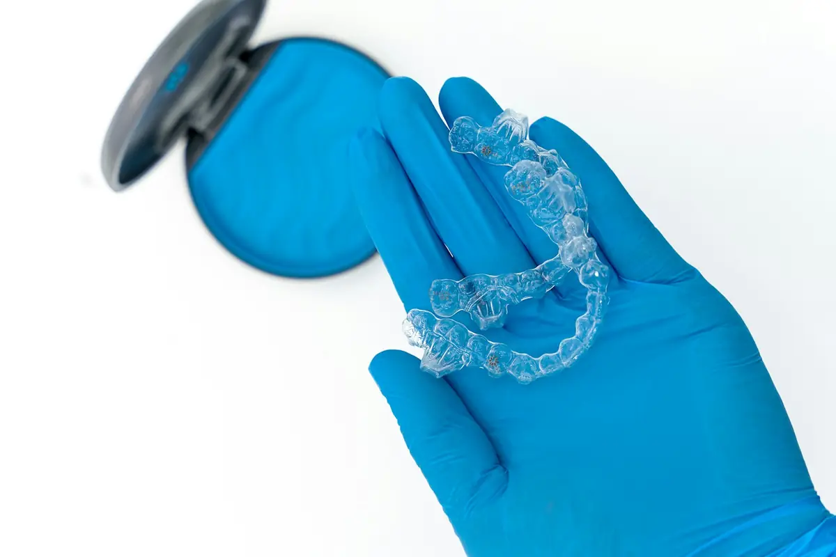 A gloved hand holding a clear custom tray beside its case